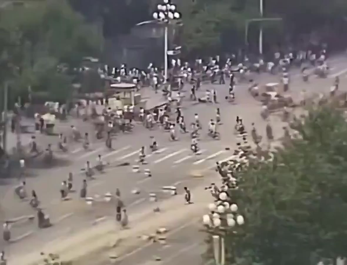 Crowds filling a wide avenue, bicycles and barricades, seen from a height.